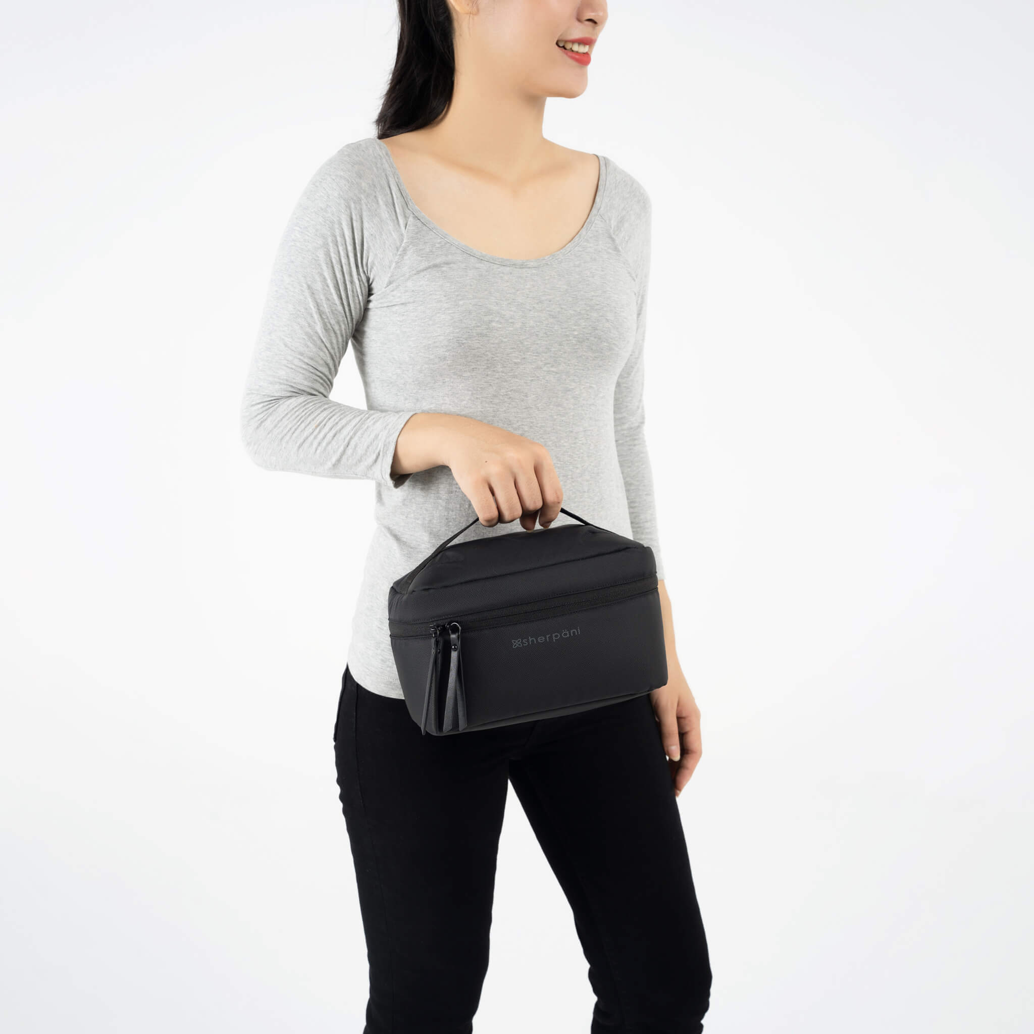 A model wearing black leggings and a gray top is holding Sherpani travel accessory the Savannah in Carbon. 