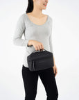 A model wearing black leggings and a gray top is holding Sherpani travel accessory the Savannah in Carbon.
