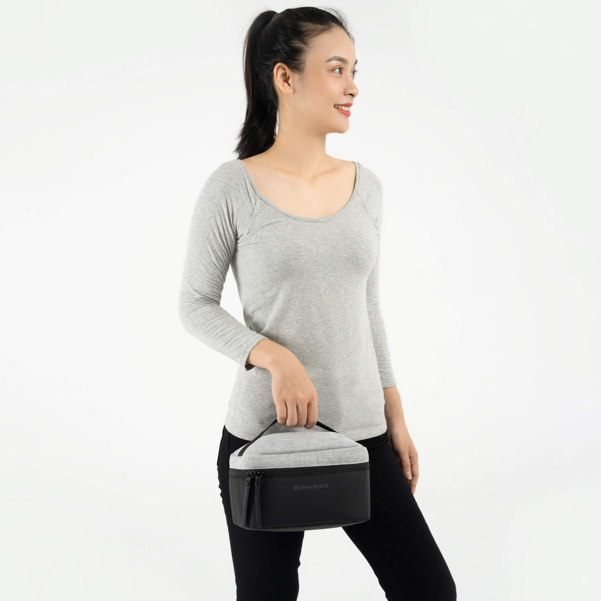 A model wearing black leggings and a gray top is holding Sherpani travel accessory the Savannah. 