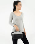 A model wearing black leggings and a gray top is holding Sherpani travel accessory the Savannah.