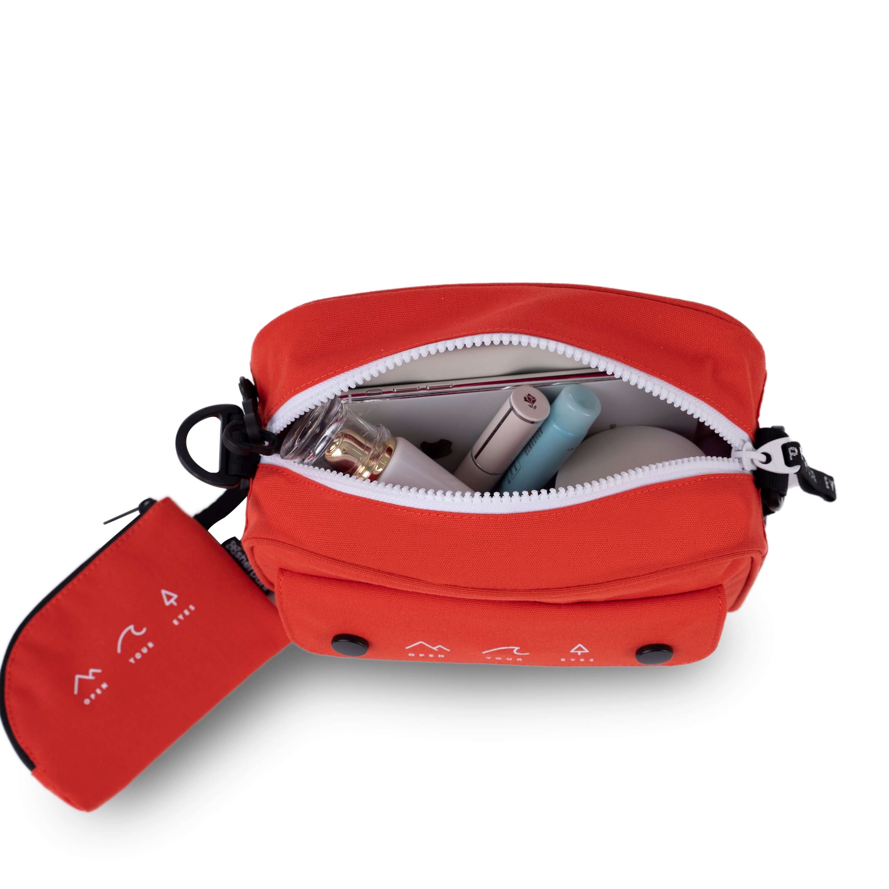 Top view of Sherpani crossbody, the Osaka in Poppy, with matching detachable coin purse. The bag is unzipped to reveal a hot pink interior. It is full of example items.