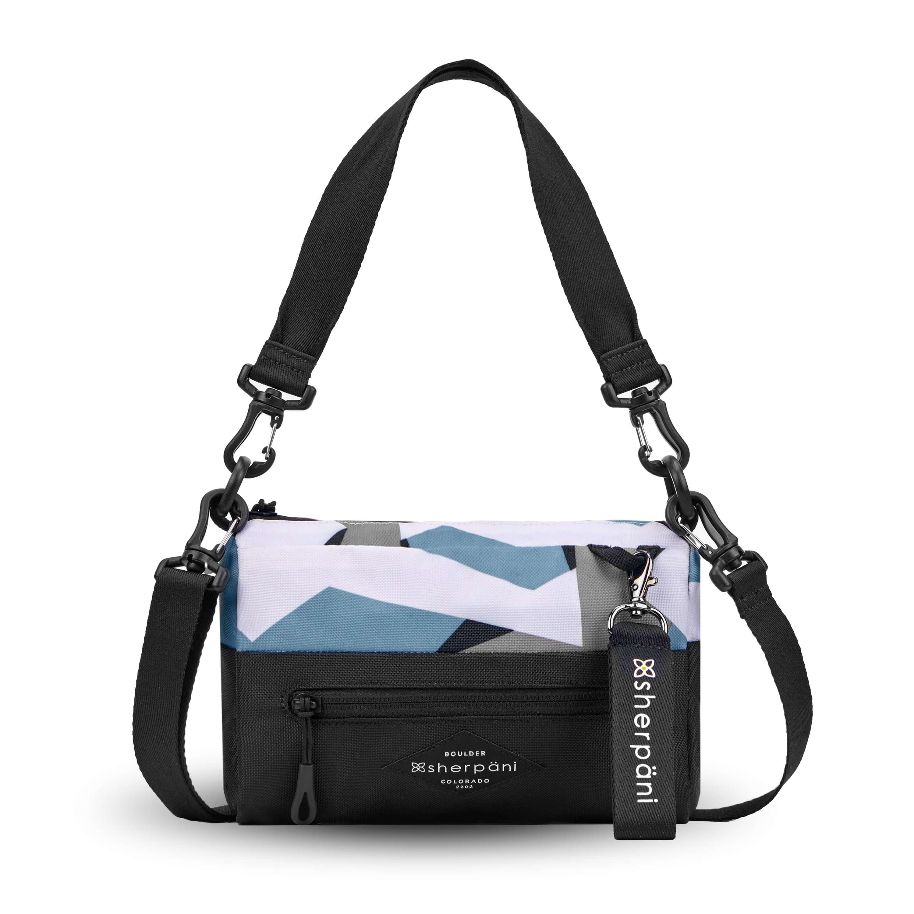 Flat front view of Sherpani's purse, the Skye in Summer Camo. It is two toned, the top half of the bag is a camouflage pattern of white, gray and blue and the bottom half of the bag is black. There is an external zipper compartment with an easy pull zipper accented in black. There is a branded Sherpani keychain clipped to the upper right corner. The bag has a detachable short strap and a longer detachable/adjustable crossbody strap. 