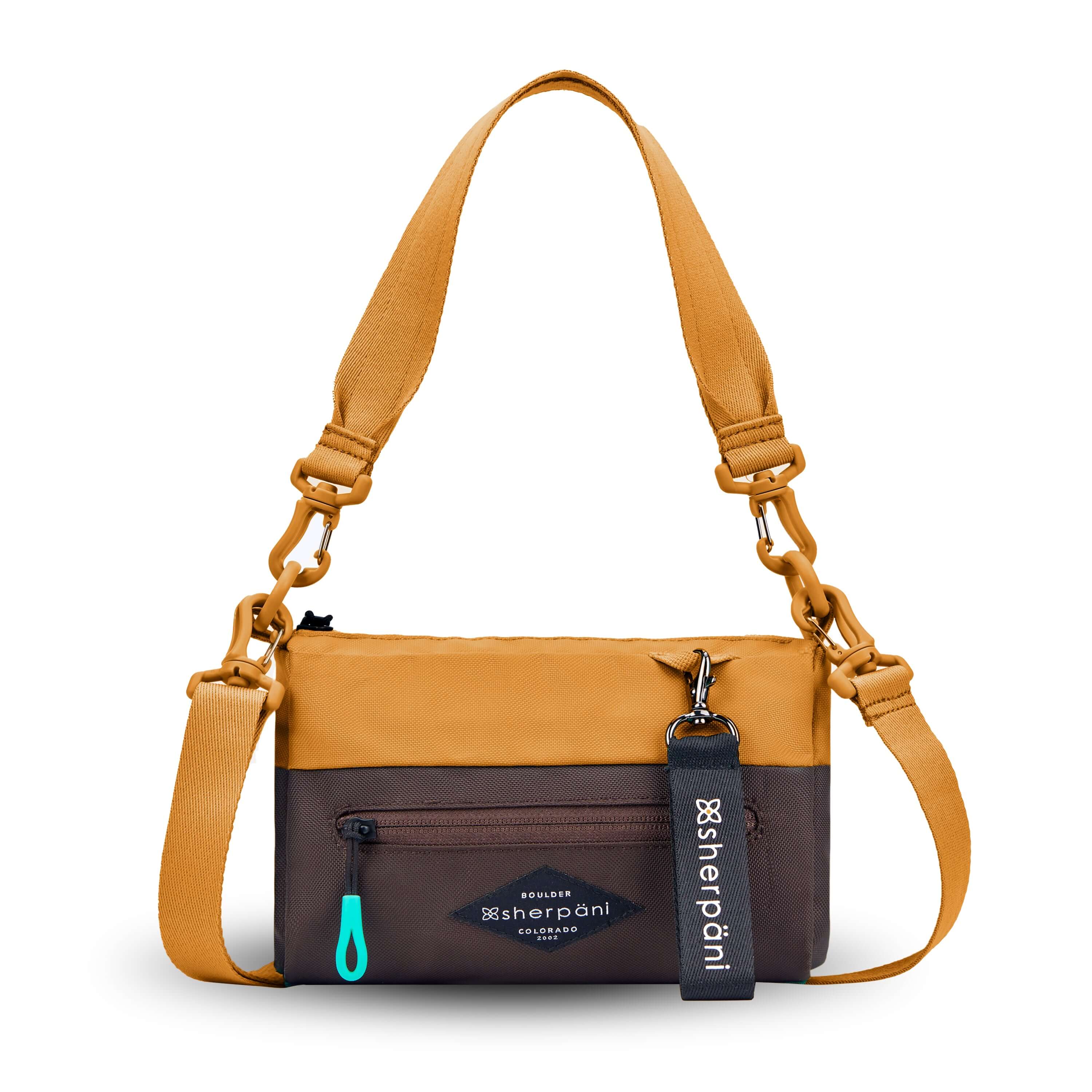 Flat front view of Sherpani's purse, the Skye in Sundial. It is two-toned, the top half of the bag is burnt yellow and the bottom half of the bag is brown. There is an external zipper compartment with an easy-pull zipper accented in aqua. There is a branded Sherpani keychain clipped to the upper right corner. The bag has a detachable short strap and a longer detachable/adjustable crossbody strap. 