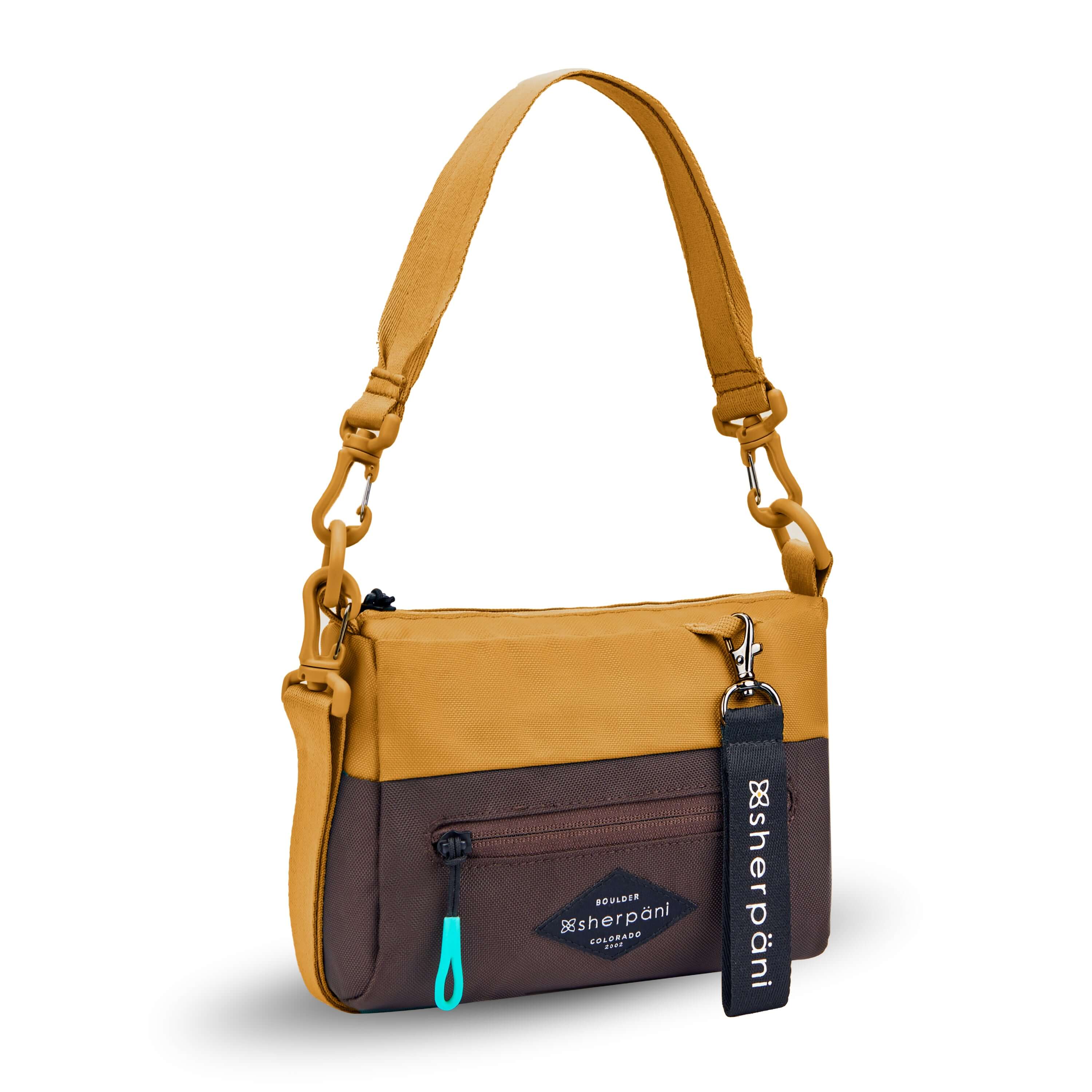 Angled front view of Sherpani's purse, the Skye in Sundial. It is two-toned, the top half of the bag is burnt yellow and the bottom half of the bag is brown. There is an external zipper compartment with an easy-pull zipper accented in aqua. There is a branded Sherpani keychain clipped to the upper right corner. The bag has a detachable short strap and a longer detachable/adjustable crossbody strap. #color_sundial-v1