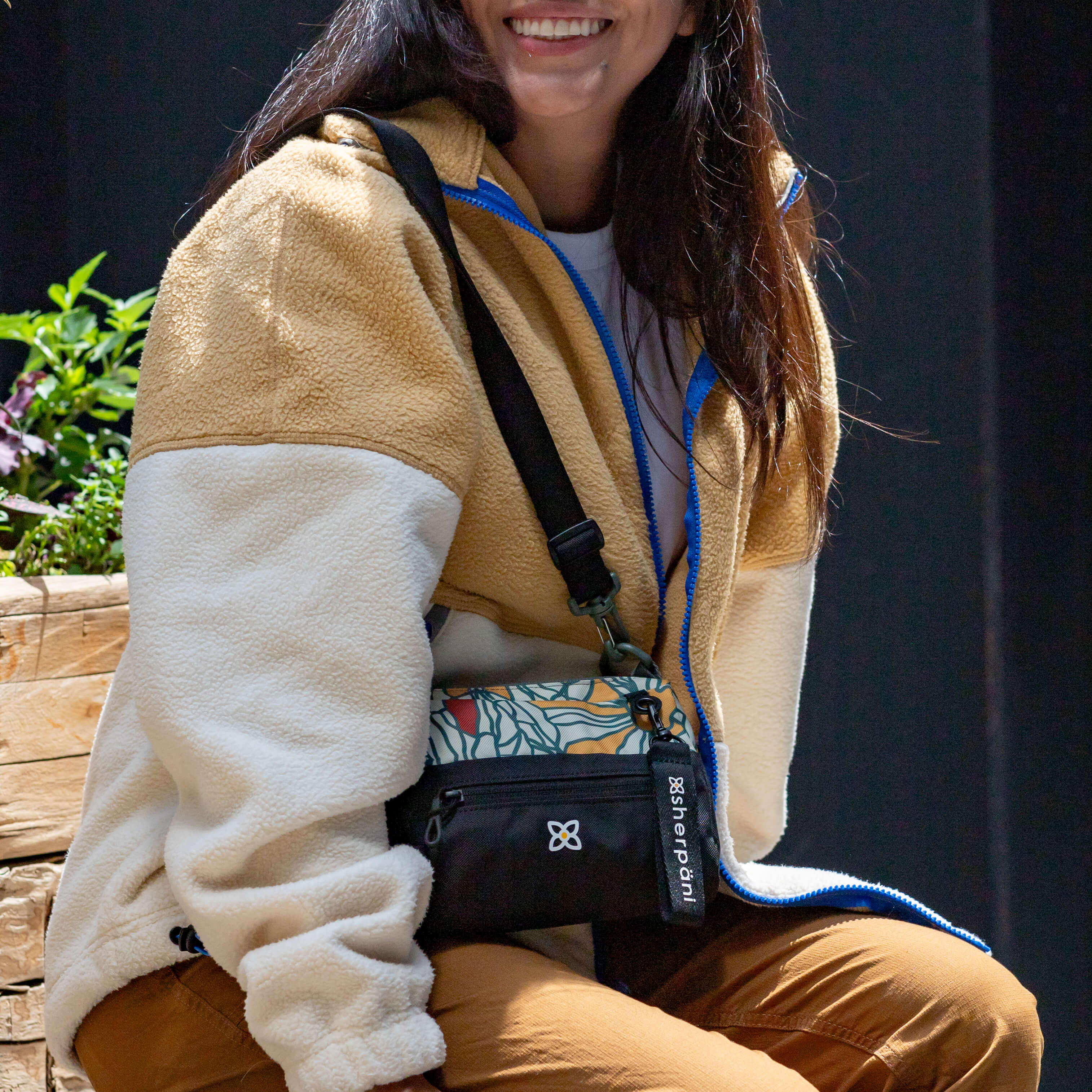A woman sits outside on a bench wearing Sherpani RFID purse, the Skye in Fiori. 