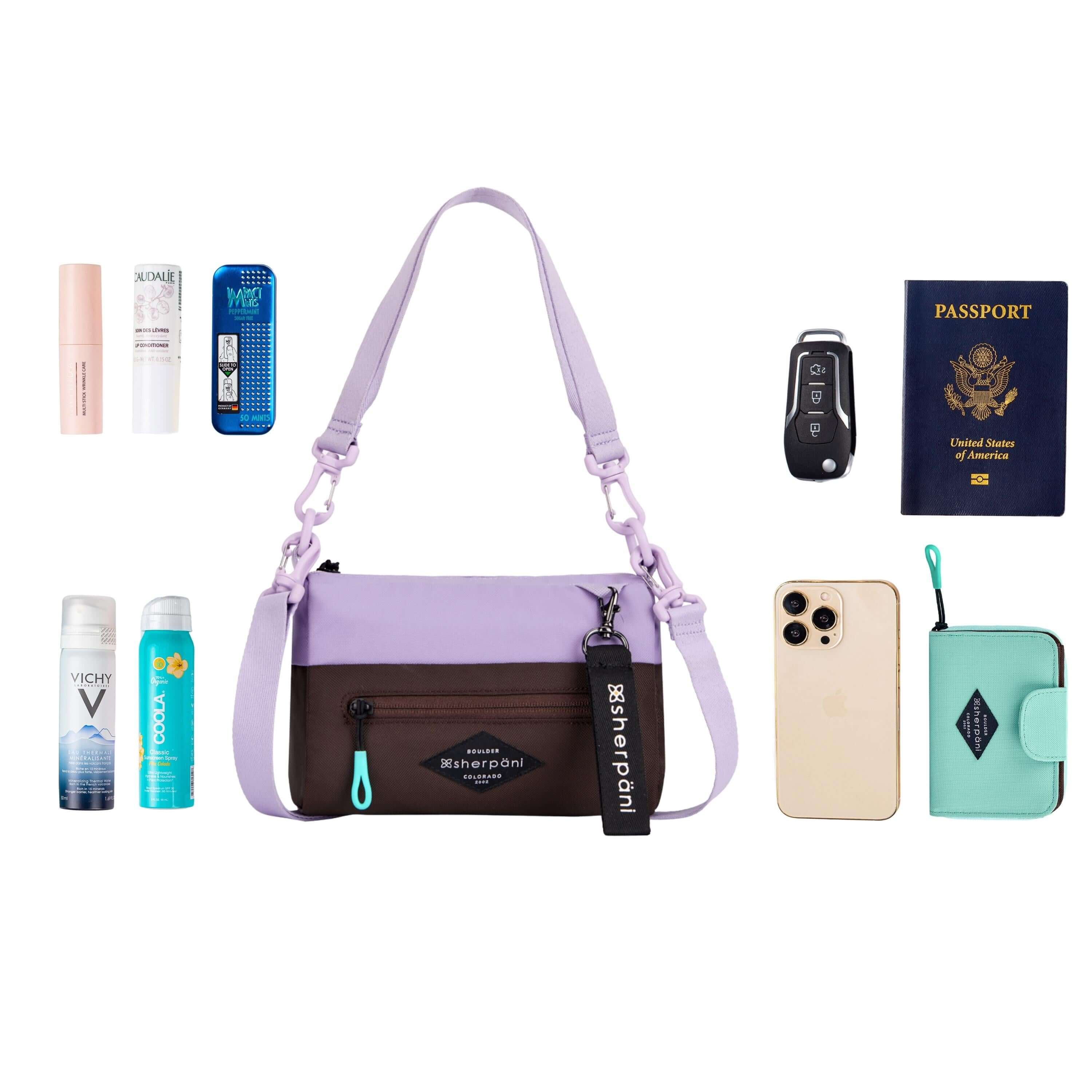 Top view of example items to fill the bag. Sherpani's purse, the Skye in Lavender, lies in the center. It is surrounded by an assortment of items: skincare products, mints, sunscreen, body spray, car key, passport, phone and Sherpani travel accessory the Barcelona in Seagreen. 