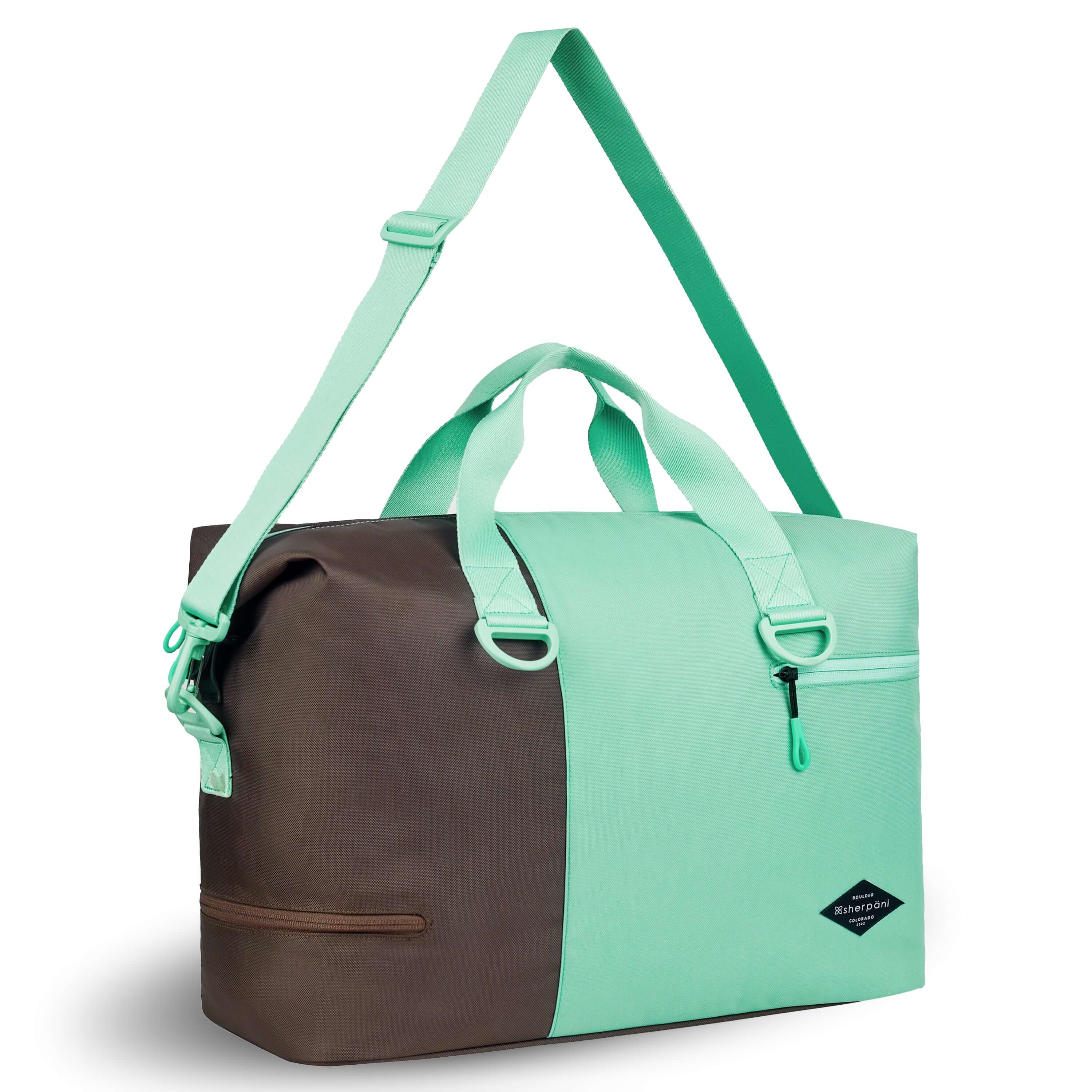 Angled front view of Sherpani bag, the Sola in Seagreen. The bag is two-toned in light green and brown. Two external zipper compartments are visible on the top right and bottom left of the bag. Easy-pull zippers are accented in light green. The bag has tote handles and an adjustable/detachable crossbody strap. #color_seagreen