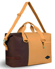 Angled front view of Sherpani bag, the Sola in Sundial. The bag is two-toned in burnt yellow and brown. Two external zipper compartments are visible on the top right and bottom left of the bag. Easy-pull zippers are accented in aqua. The bag has tote handles and an adjustable/detachable crossbody strap.