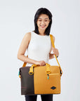 Close up view of a dark haired model facing the camera and smiling downward. She is wearing a white tank top and black leggings. She carries Sherpani bag, the Sola in Sundial, as a crossbody.