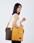 Close up view of a dark haired model facing the side and smiling over her right shoulder. She is wearing a white tank top and black leggings. She carries Sherpani bag, the Sola in Sundial, as a crossbody.