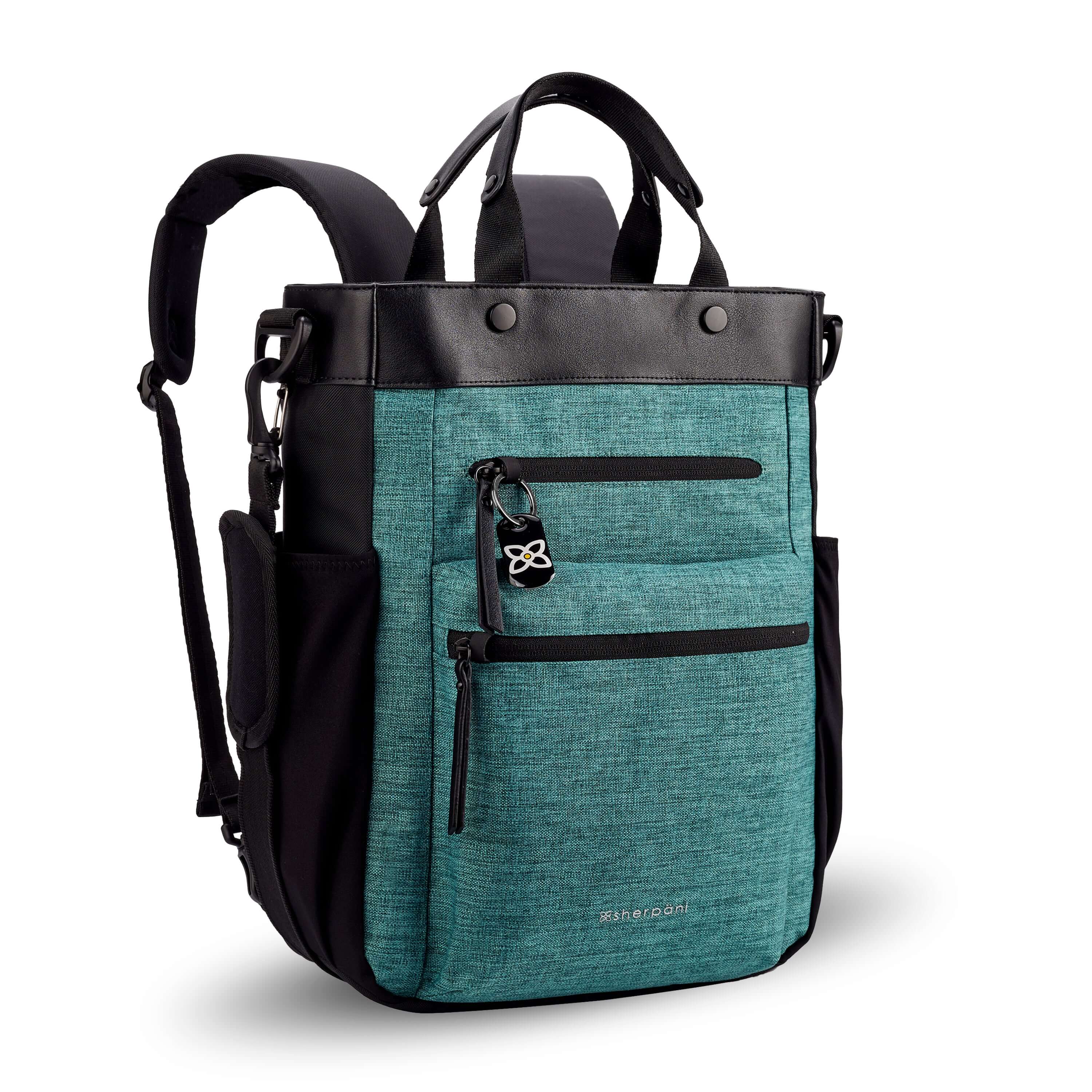 Angled front view of Sherpani's Anti-Theft bag, the Soleil AT in Teal, with vegan leather accents in black. On the front are two locking zipper compartments, a ReturnMe tag is clipped to the upper one. Two elastic water bottle holders sit on either side of the bag. It has padded backpack straps, short tote handles, and an adjustable/detachable crossbody strap. 