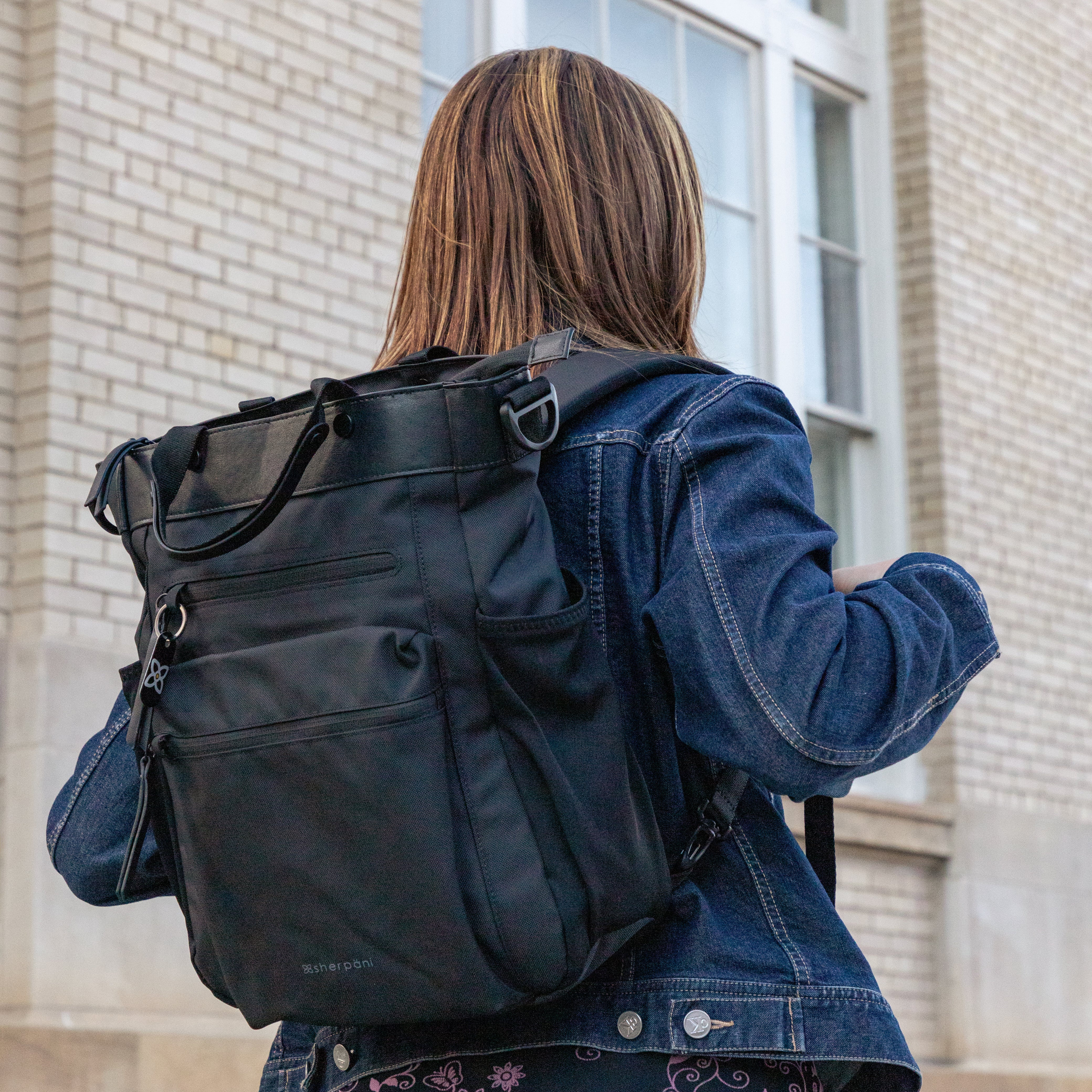 A woman standing outside wearing Sherpani Anti-Theft travel bag, the Soleil in Carbon, as a backpack. 