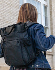 A woman standing outside wearing Sherpani Anti-Theft travel bag, the Soleil in Carbon, as a backpack.