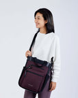 Close up view of a dark haired model facing the camera and smiling. She is wearing a white sweatshirt, purple leggings, and Sherpani’s Anti-Theft bag, the Soleil AT in Merlot, as a crossbody.