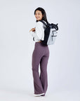 Full body view of a dark haired model facing away from the camera and smiling over her left shoulder. She is wearing a white sweatshirt, purple leggings and Sherpani’s Anti-Theft bag, the Soleil AT in Sterling, as a backpack.