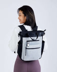 Close up view of a dark haired model facing away from the camera and smiling over her left shoulder. She is wearing a white sweatshirt, purple leggings and Sherpani’s Anti-Theft bag, the Soleil AT in Sterling, as a backpack.