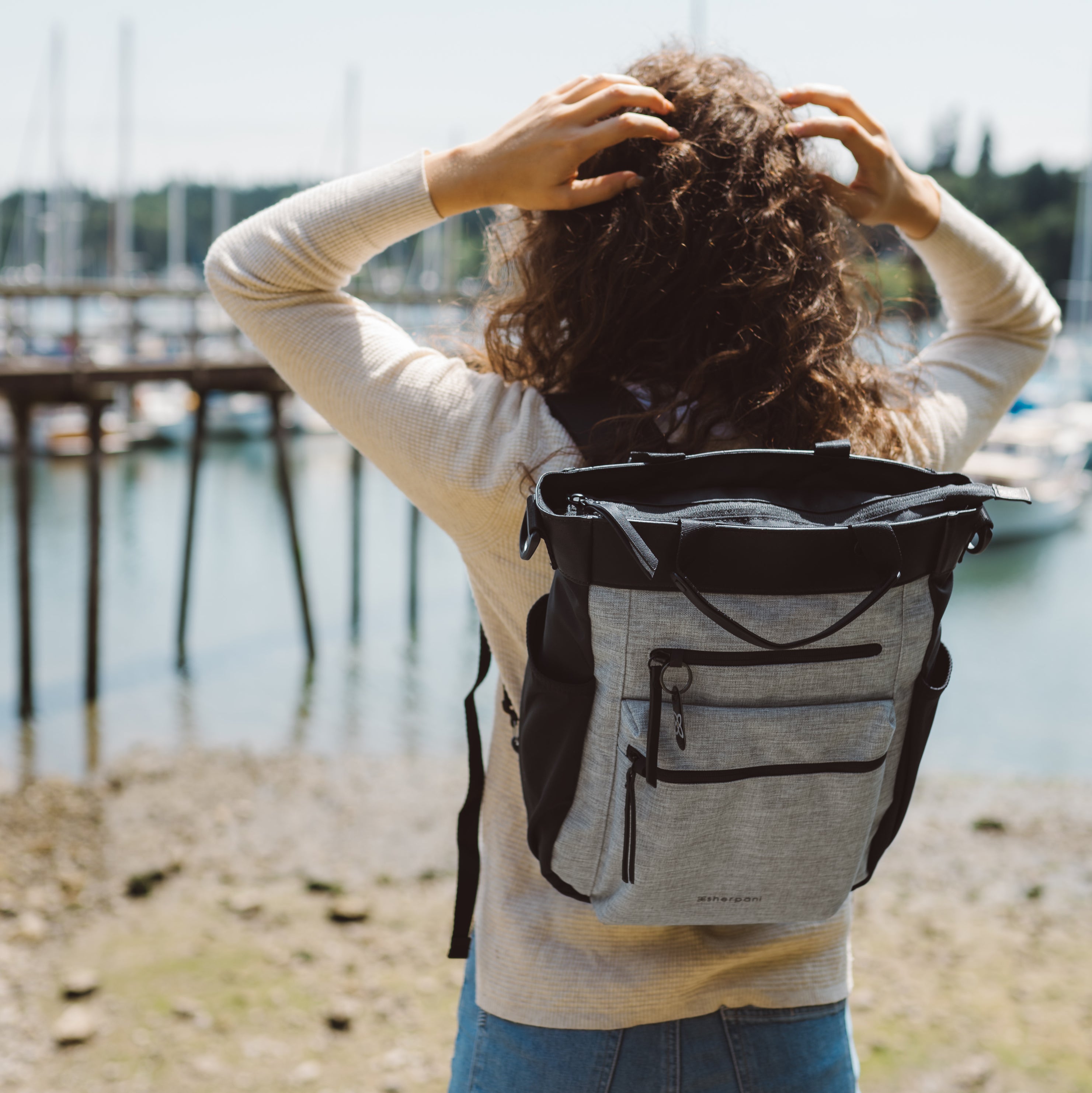 A woman stands facing a waterfront wearing Sherpani Anti-Theft travel back, the Soleil in Sterling, as a backpack.