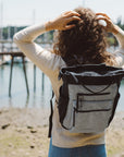 A woman stands facing a waterfront wearing Sherpani Anti-Theft travel back, the Soleil in Sterling, as a backpack.
