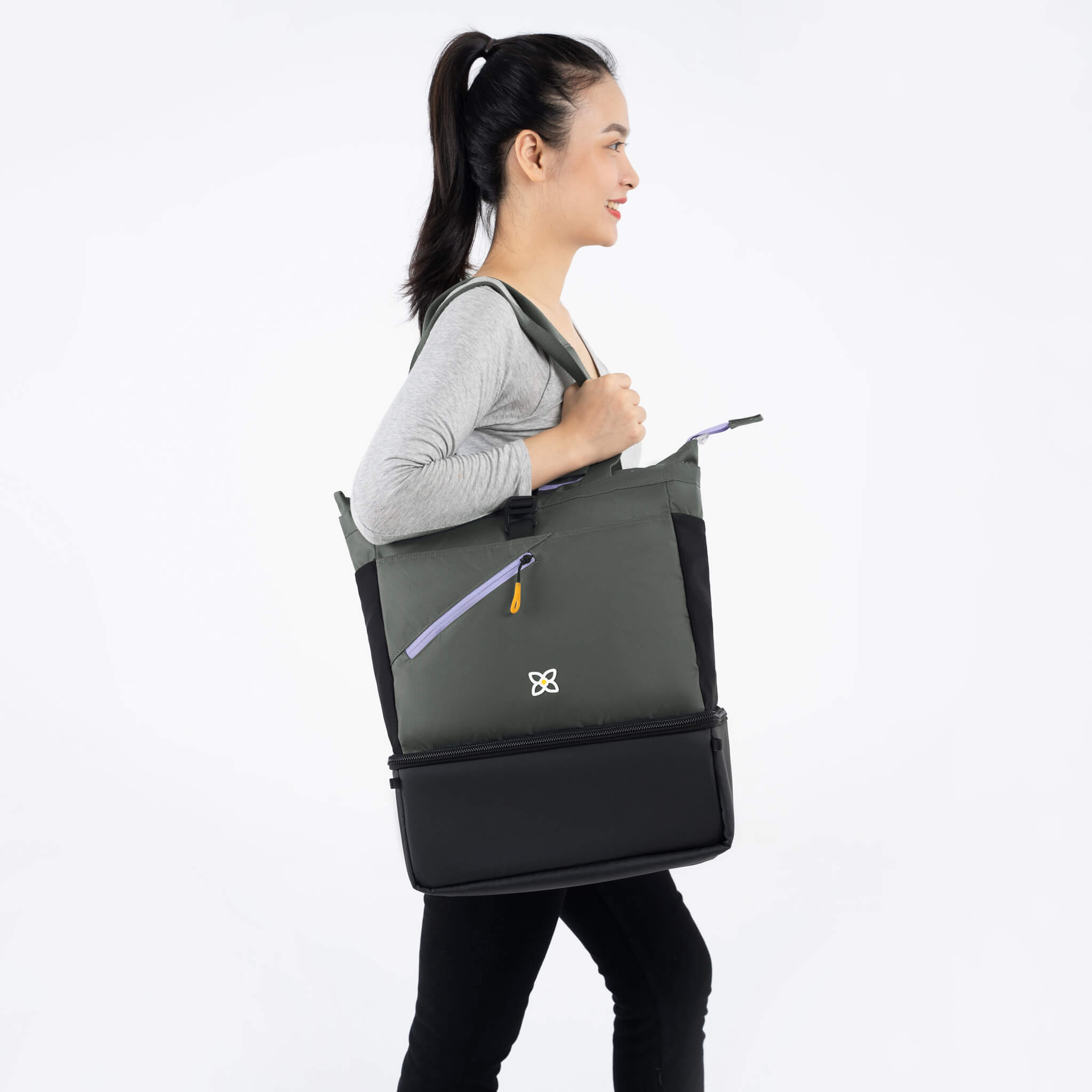 A model facing to the side. She is wearing a gray top and black leggings. She carries Sherpani bag, the Terra in Juniper, as a tote on her shoulder. 