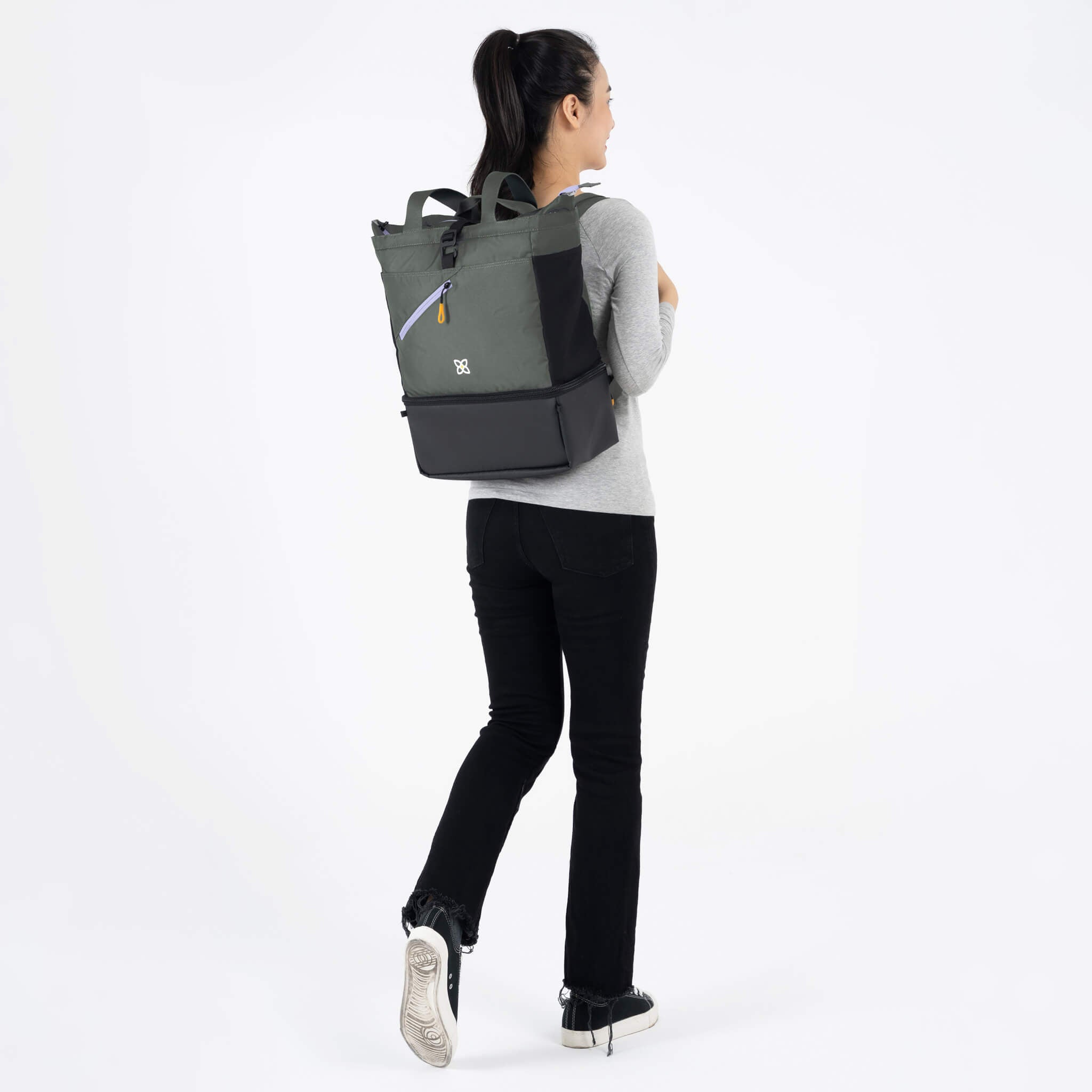 A model facing to the back. She is wearing a gray top and black leggings. She carries Sherpani bag, the Terra in Juniper, as a backpack. 