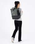 A model facing to the back. She is wearing a gray top and black leggings. She carries Sherpani bag, the Terra in Juniper, as a backpack.