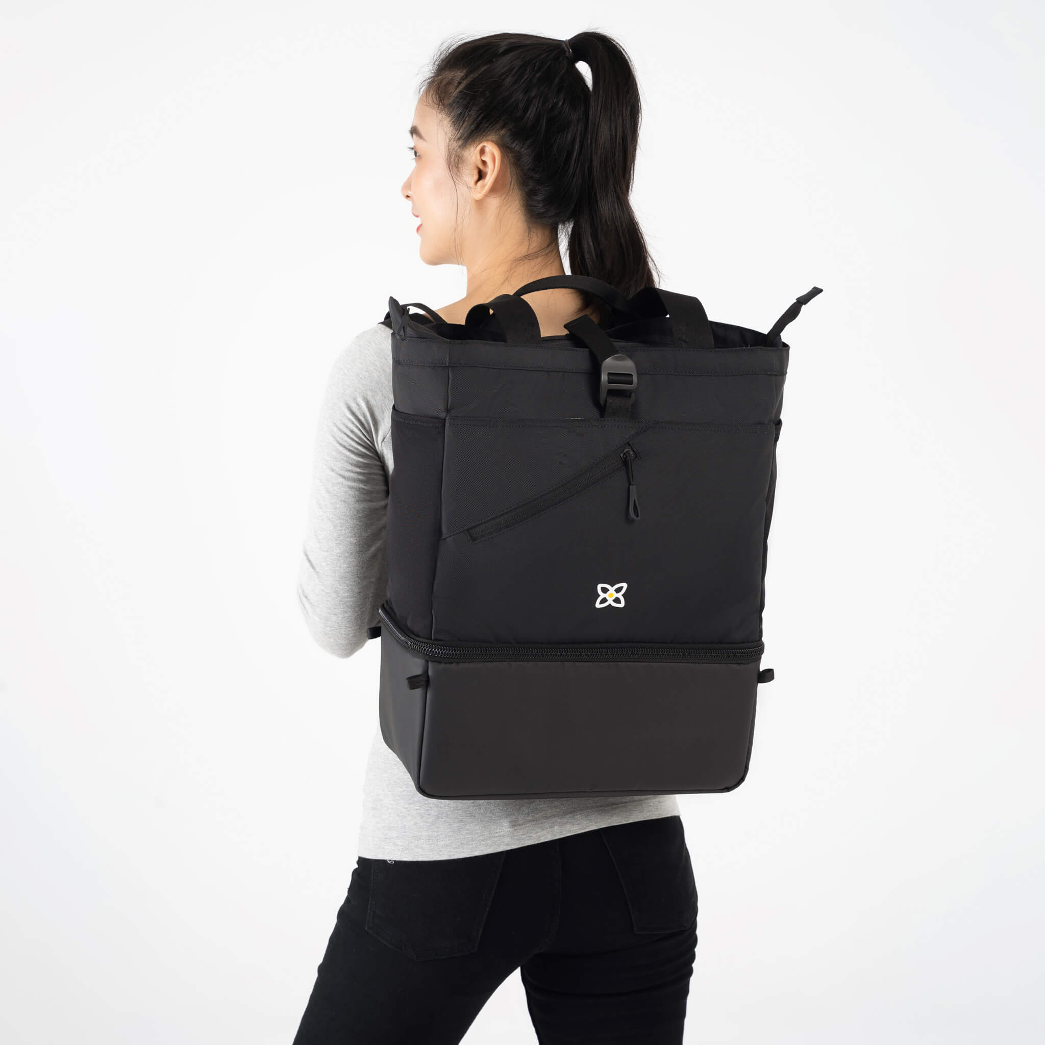A model facing to the back. She is wearing a gray top and black leggings. She carries Sherpani bag, the Terra in Raven, as a backpack. 