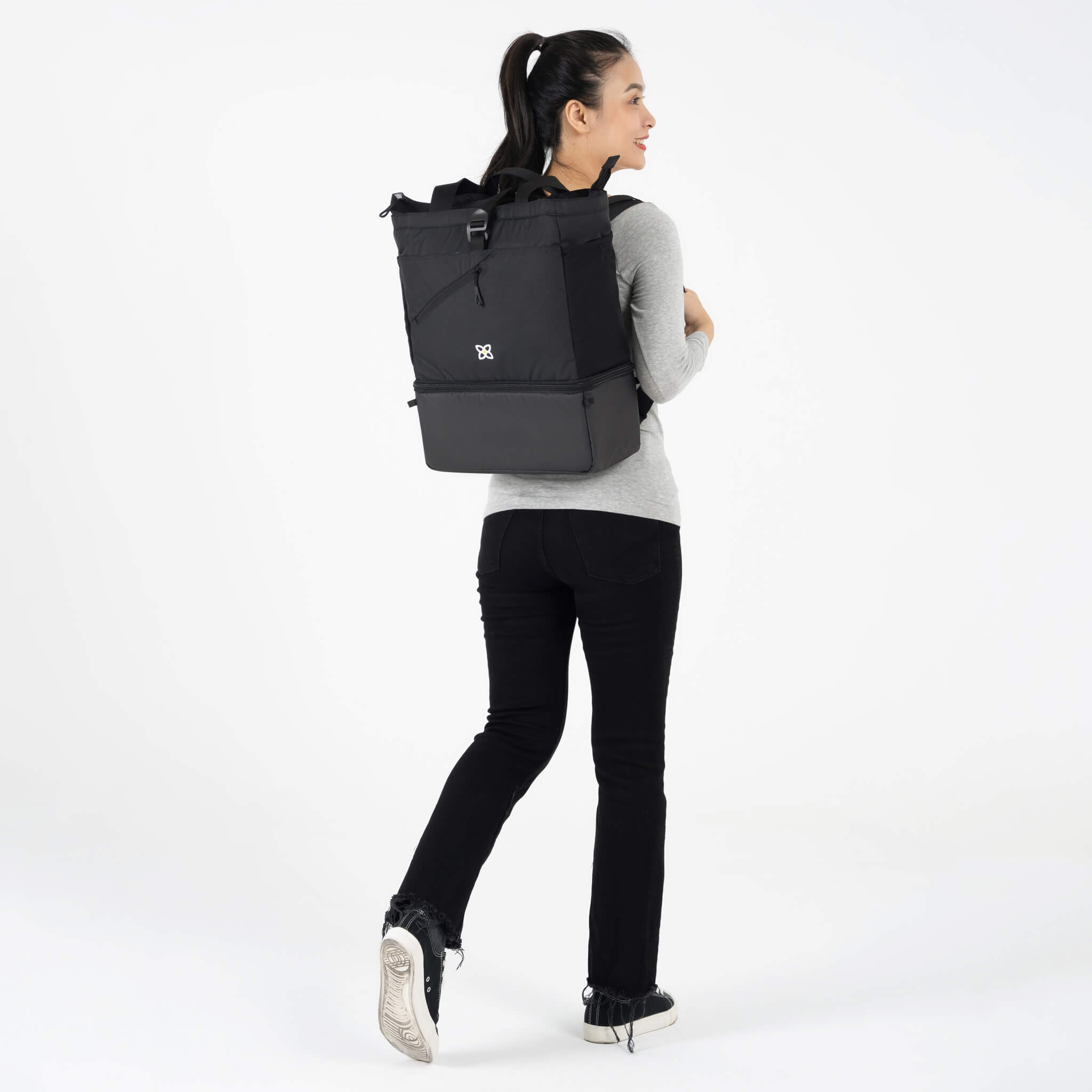 A model facing to the back. She is wearing a gray top and black leggings. She carries Sherpani bag, the Terra in Raven, as a backpack. 