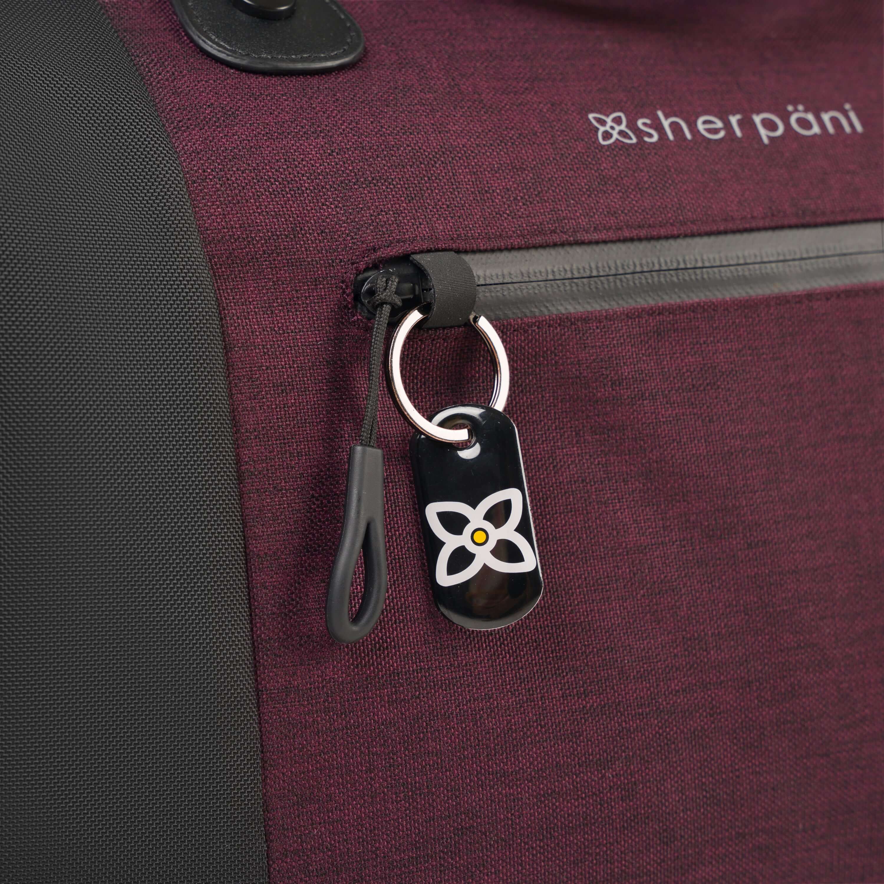 Close up view of locking zipper compartment and ReturnMe tag on Sherpani&#39;s Anti-Theft rolling duffle the Tip in Merlot.