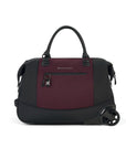 Flat front view of Sherpani’s Anti Theft rolling Duffle, the Trip in Merlot, with vegan leather accents in black.  The bag lies flat on the ground with a retractable luggage handle hidden on the left side and the rolling wheels shown on the right side. The bag features short tote handles at the top and an external zipper compartment on the front panel with locking zipper and ReturnMe tag.