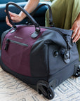 Close up view of Sherpani rolling duffle bag, the Trip in Merlot. Trip features include tote bag handles, retractable luggage handle, internal mesh pocket, internal zipper pocket, two external zipper pockets, Anti-Theft features and rolling wheels.