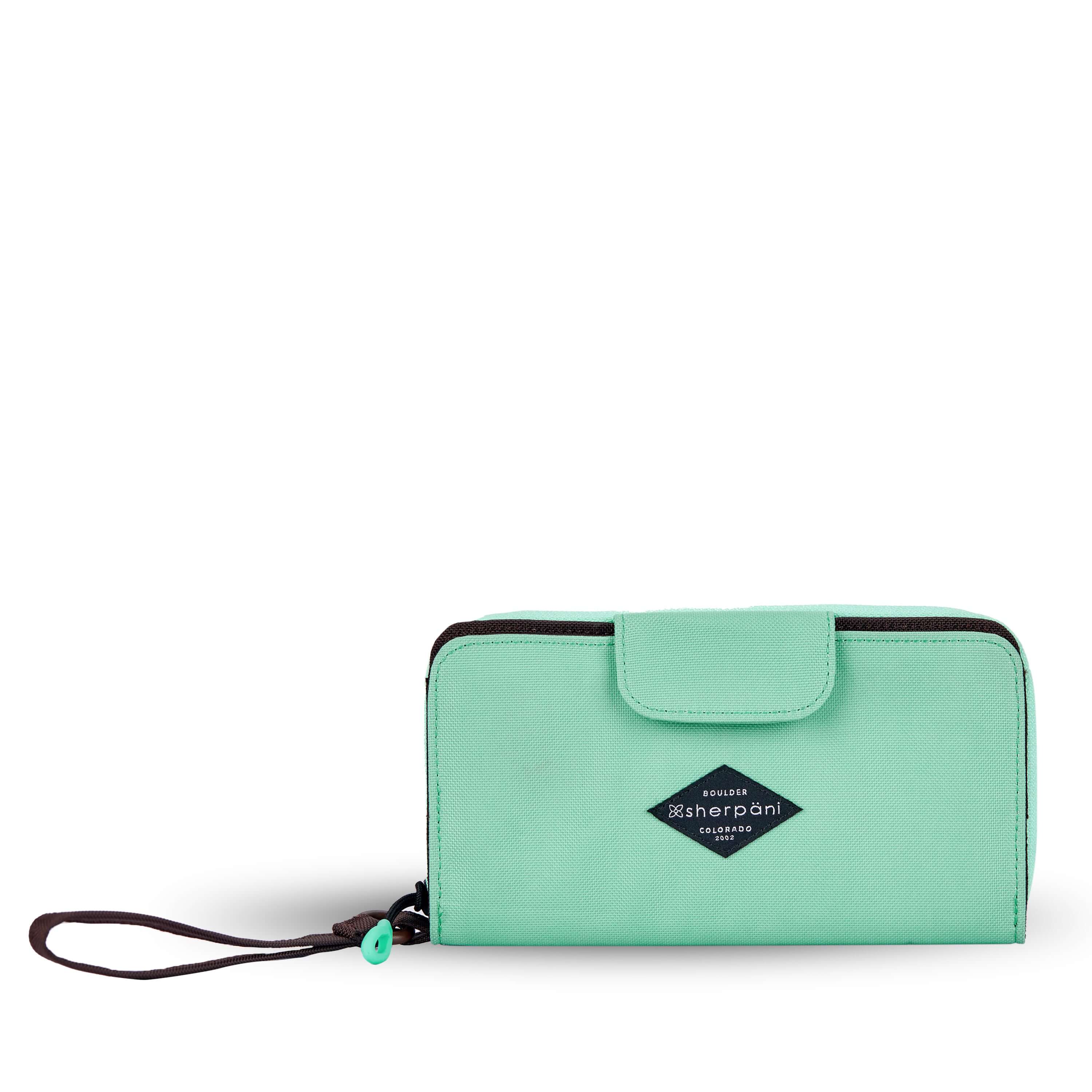 Flat front view of Sherpani wallet, the Tulum in Seagreen. The wallet is light green in color. There is a fabric flap with snap feature that folds over to open and close the wallet. There is a zipper compartment in the back with an easy-pull zipper accented in light green. The wallet features a wristlet strap in brown.