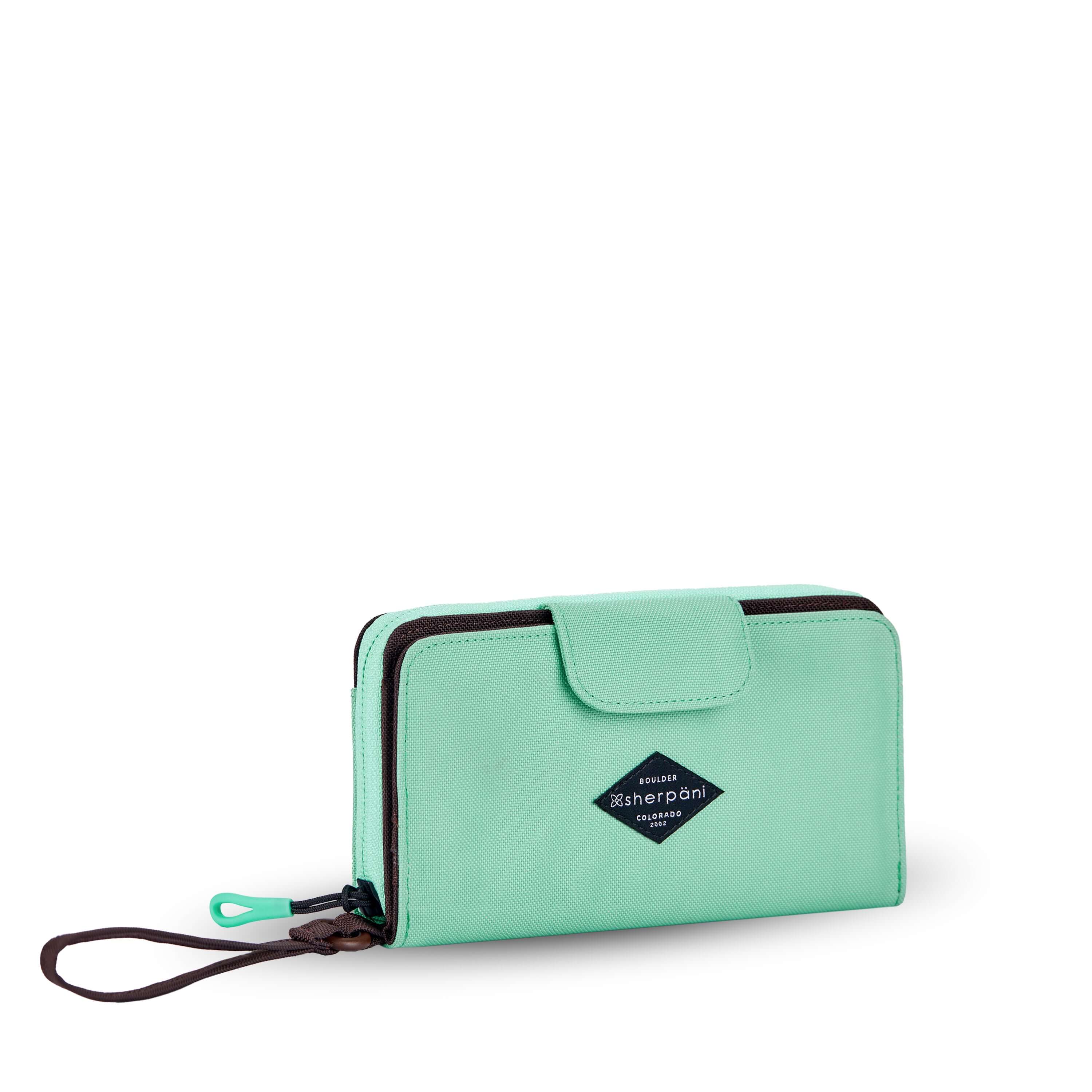Angled front view of Sherpani wallet, the Tulum in Seagreen. The wallet is light green in color. There is a fabric flap with snap feature that folds over to open and close the wallet. There is a zipper compartment in the back with an easy-pull zipper accented in light green. The wallet features a wristlet strap in brown.