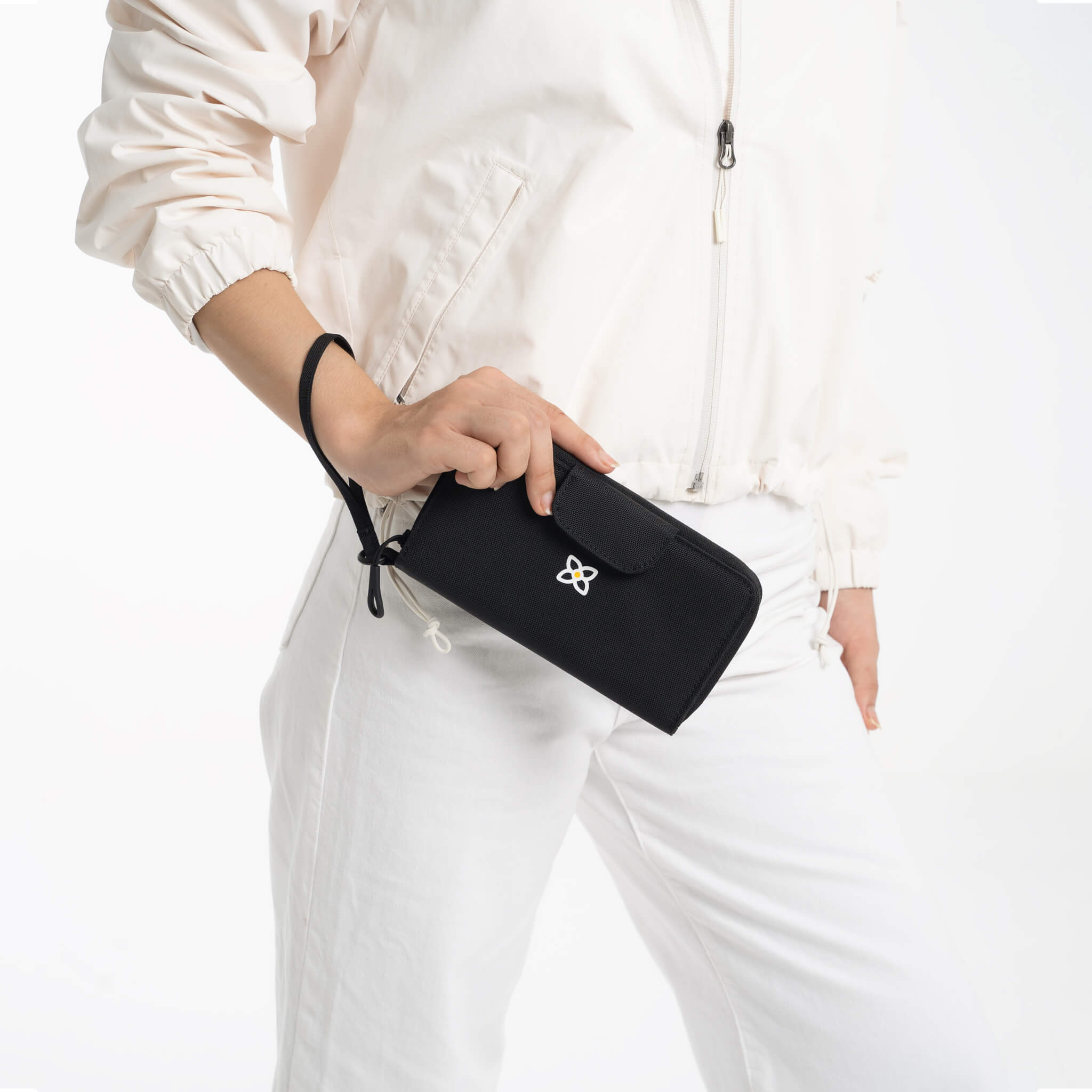 A model holding Sherpani travel wallet with RFID protection, the Tulum in Raven. The wristlet strap is around her wrist. 