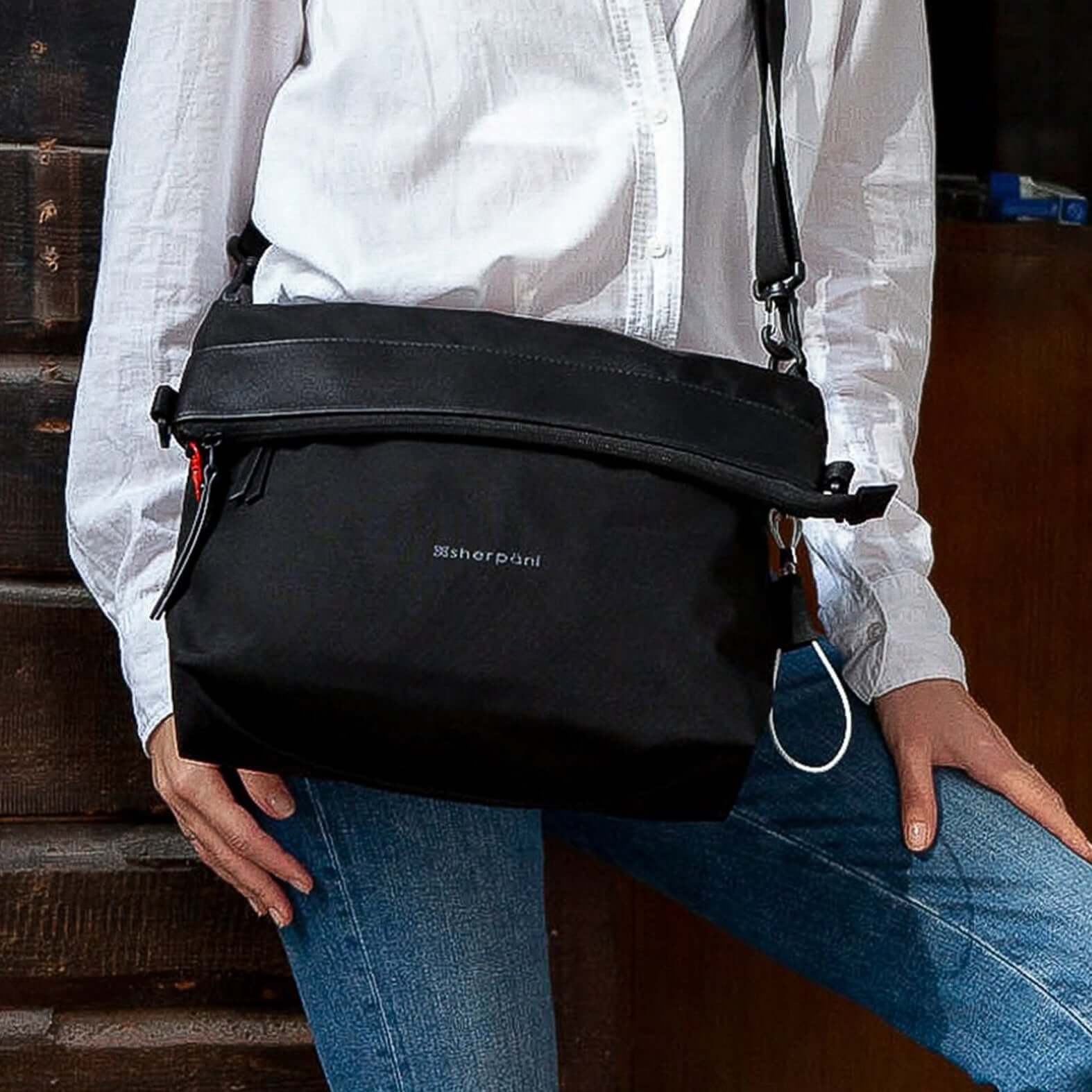 Close up view of a model wearing a long sleeved white shirt and blue jeans. She is wearing Sherpani's Anti-Theft bag, the Vale AT in Carbon, as a crossbody. 