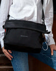 Close up view of a model wearing a long sleeved white shirt and blue jeans. She is wearing Sherpani's Anti-Theft bag, the Vale AT in Carbon, as a crossbody.