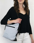 Close up view of a model facing the camera and smiling. She is wearing a black shirt and white pants. She carries Sherpani's Anti-Theft bag, the Vale AT in Sterling, over her shoulder as a tote.