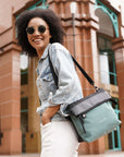 Close up view of a curly haired model looking over her left shoulder and smiling at the camera. She is wearing sunglasses, a jean jacket, white pants and Sherpani's Anti-Theft bag, the Vale AT in Teal, over her shoulder.