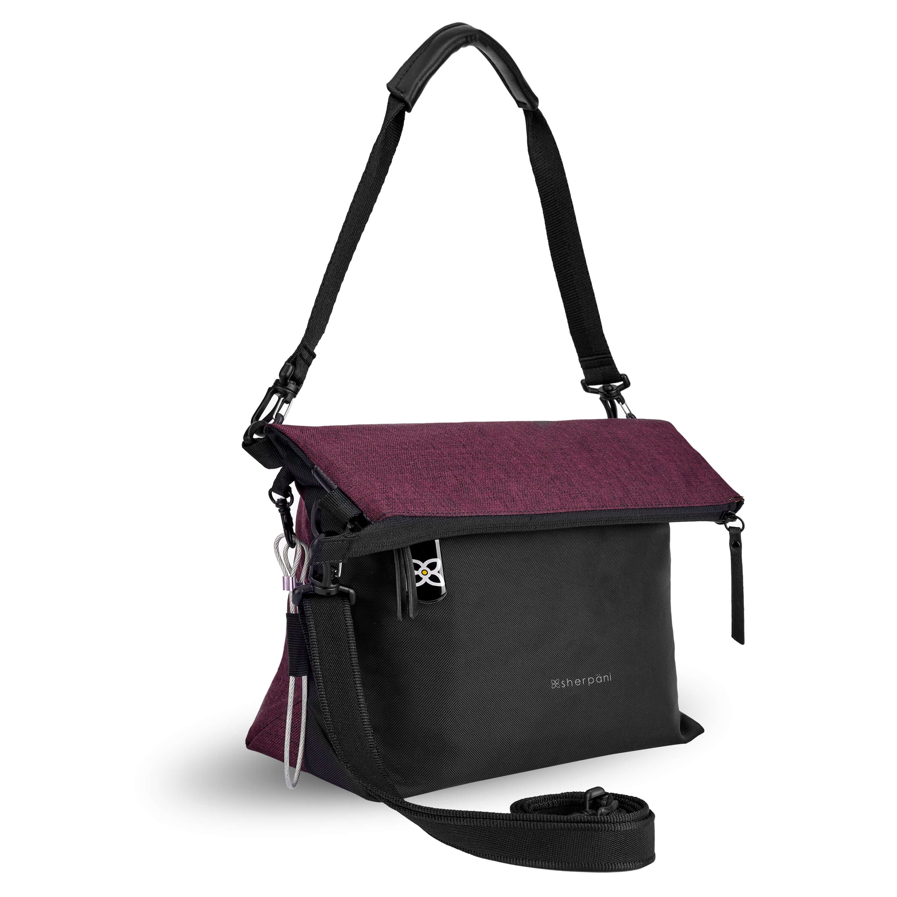 Angled front view of Sherpani's Anti-Theft bag, the Vale AT in Merlot with vegan leather accents in black. The top is folded over creating a signature overlap look. A chair loop lock is connected to a key fob clip on one side. It has an adjustable/detachable crossbody strap, and a second detachable strap fixed at a shorter length.