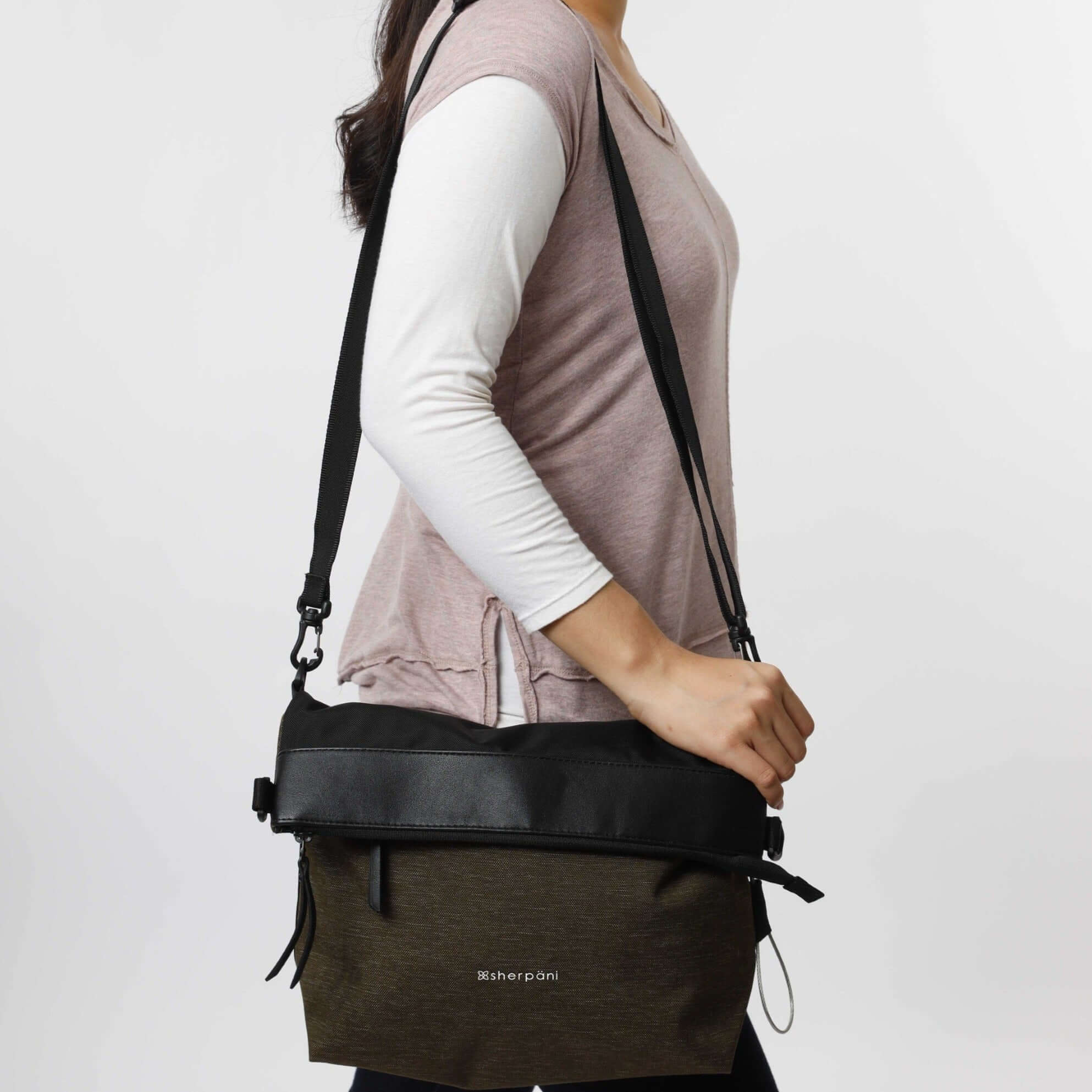 Close up view of a brown haired model. She is wearing a long sleeved white and pink shirt and Sherpani&#39;s Anti-Theft bag, the Vale AT in Loden, over her shoulder.
