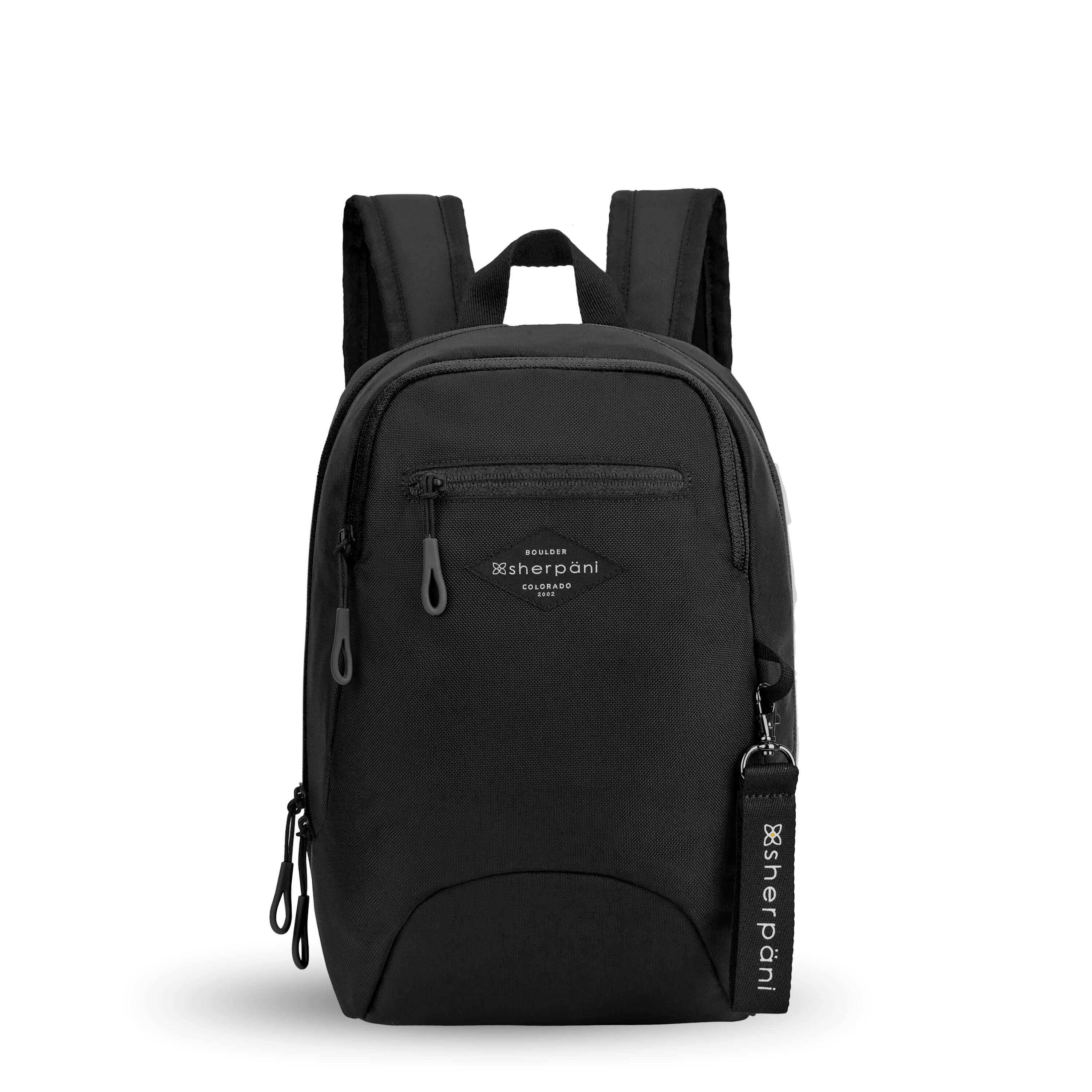 Flat front view of Sherpani mini backpack, the Vespa in Raven. The bag is black in color and features easy-pull zippers accented in black. It has padded and adjustable backpack straps, as well as a tote handle for easy carrying. The bag has a main zipper compartment, a smaller secondary zipper compartment and an external zipper pocket on the front. A branded Sherpani keychain is clipped to a fabric loop on the front of the bag.