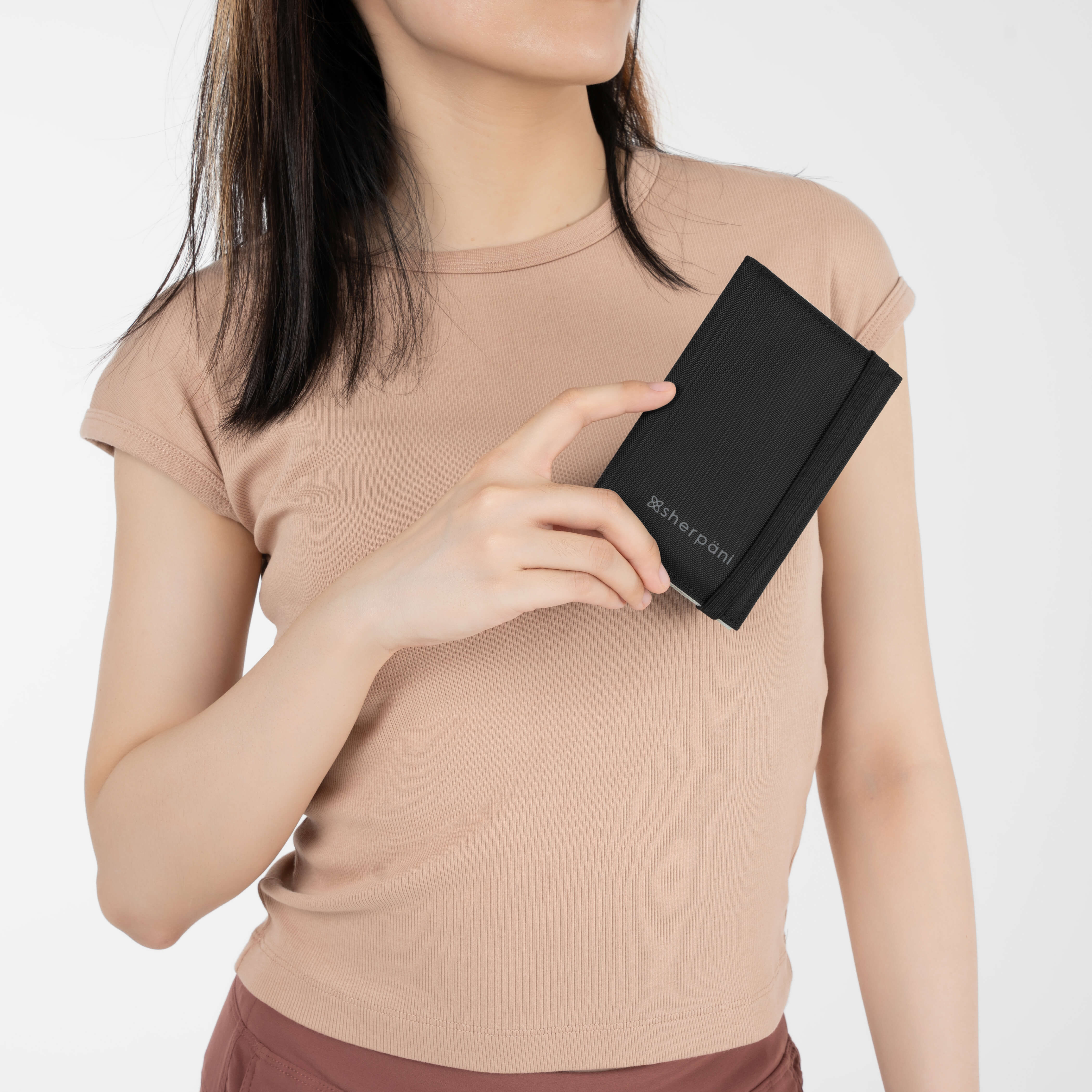 Model holding Sherpani travel wallet for passport protection, the Vienna in Carbon. 