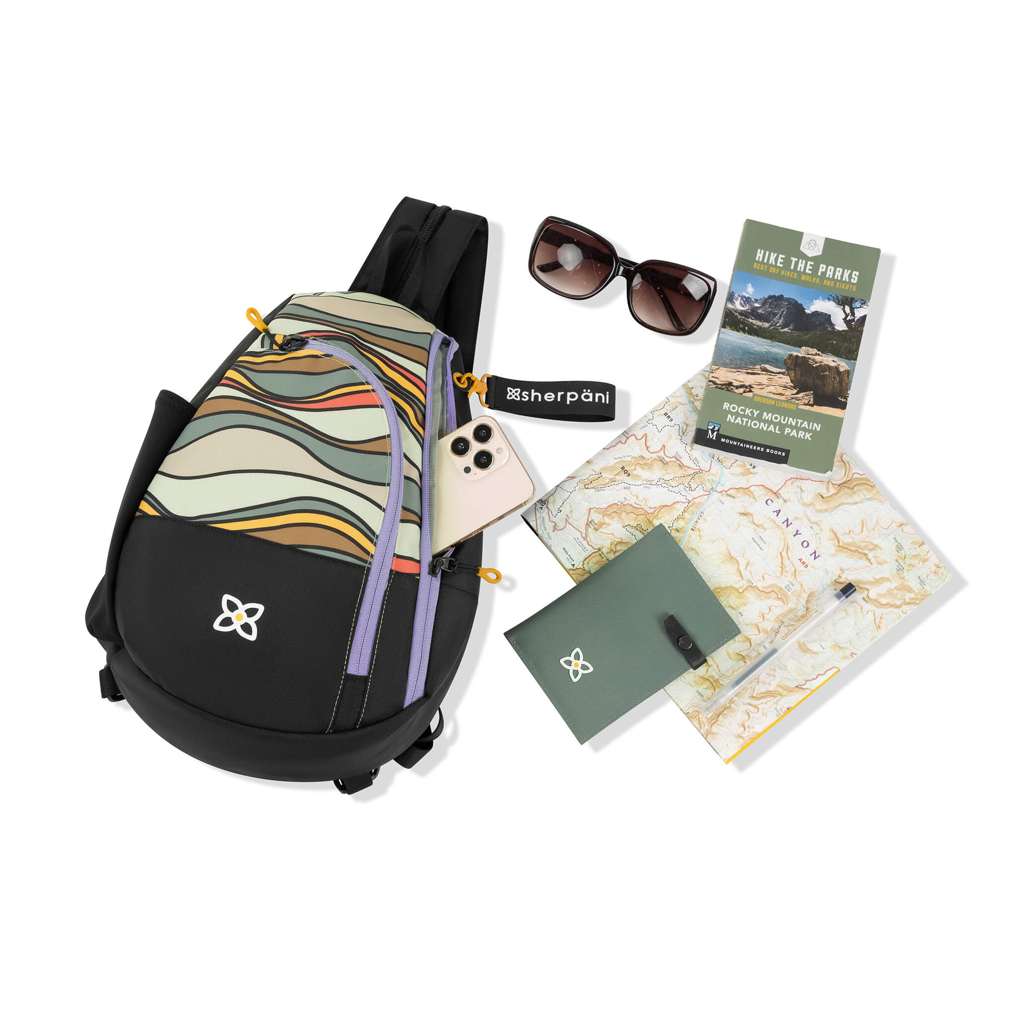 Sherpani women's sling bag for travel the Wayfarer, surrounded by example items for packing. 