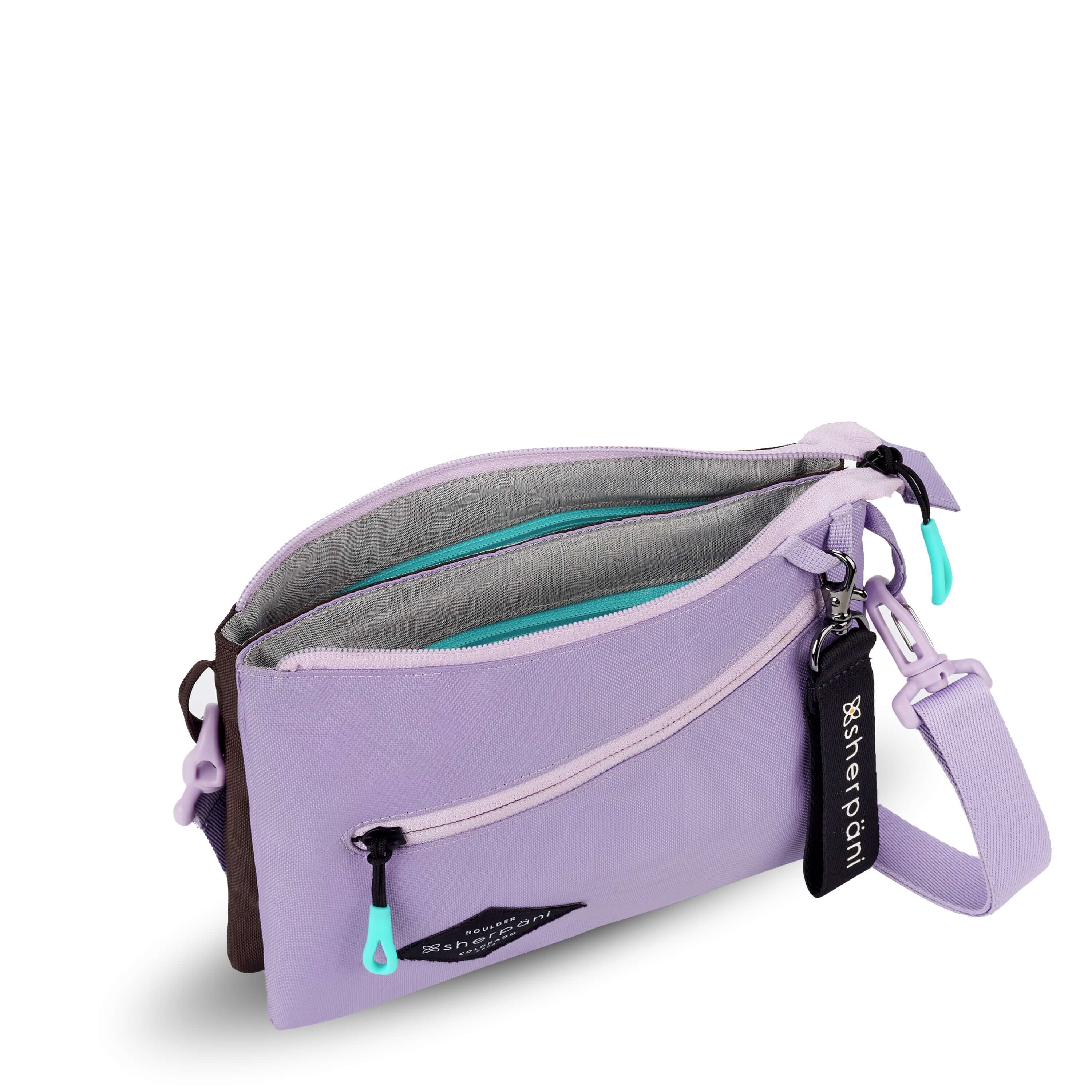 Top view of Sherpani crossbody, the Zoom in Lavender. The main zipper compartment is open to reveal an internal divider that separates the bag into dual compartments. The inside of the bag is light gray with zipper pockets accented in aqua.