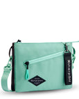 Angled front view of Sherpani crossbody, the Zoom in Seagreen. The bag is two-toned; the front half is light gray and the back half is brown. There is an external zipper pocket on the front with an easy-pull zipper accented in light green. The bag has an adjustable/detachable crossbody strap. There is a branded Sherpani keychain clipped to a fabric loop on the upper right corner.