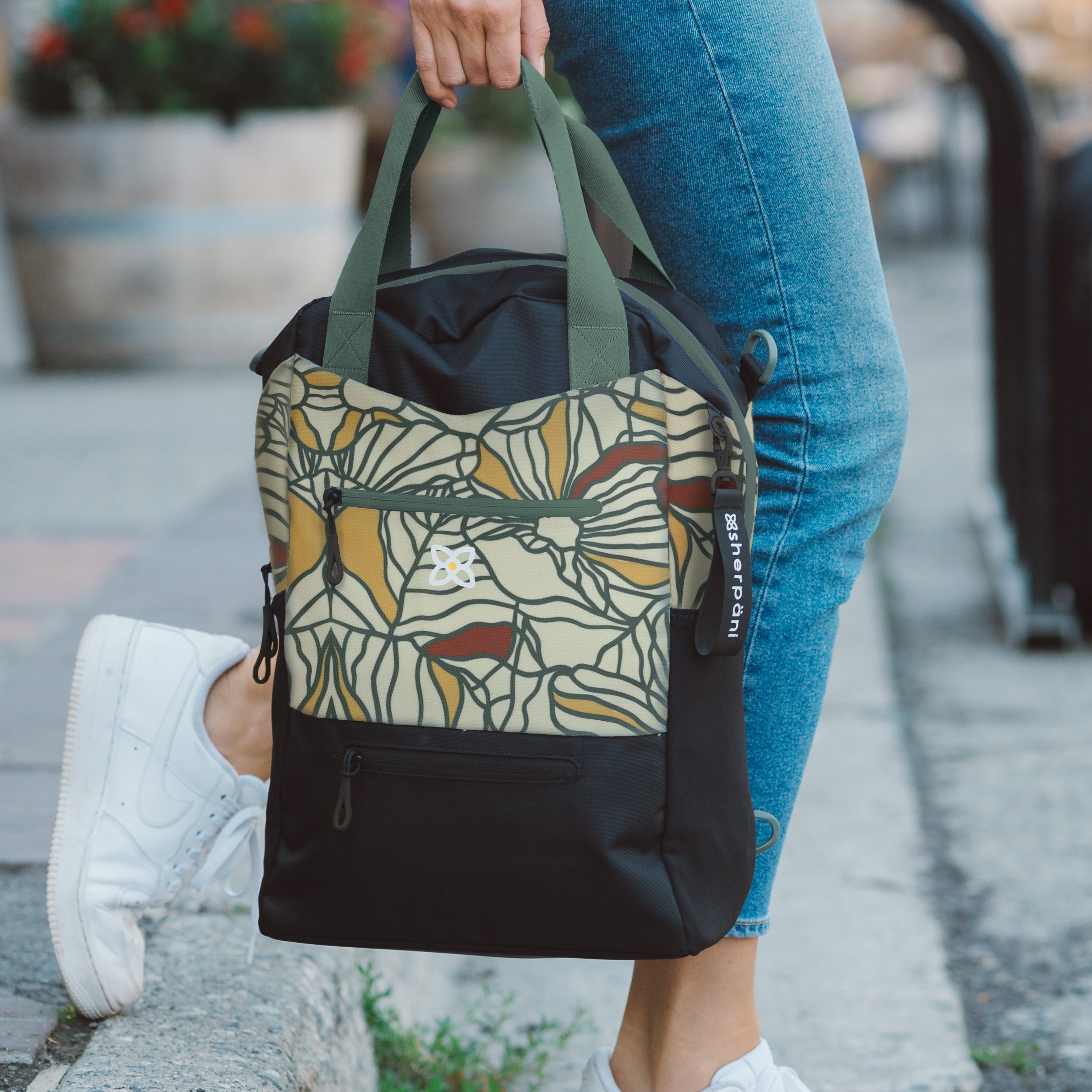 A woman carrying Sherpani travel tote, the Camden in Fiori, by the fixed tote bag handles. 