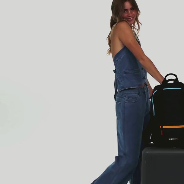 A woman shows the features of a
Sherpani Camden Chromatic Black Backpack, such as the luggage strap.