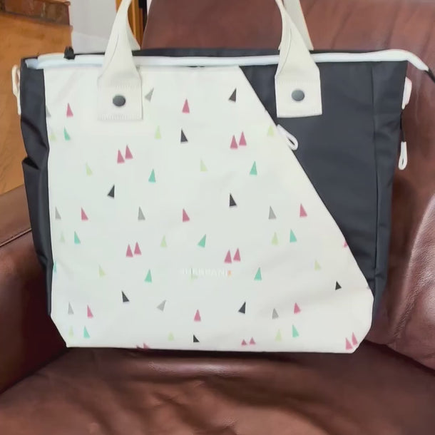 A woman packs a Sherpani Jetsetter Terrazzo Print Travel Tote Bag with various items, such as a laptop, water bottle, and more. 