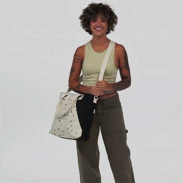 A woman shows features of Sherpani Jetsetter Terrazzo Print Travel Tote Bag, such as a water bottle pocket and a luggage strap.