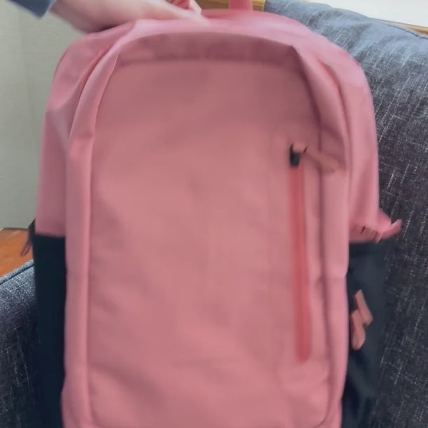 A woman packs a Sherpani Desert Pink Travel Backpack with various items, including a laptop, keys, notebooks, and more.
