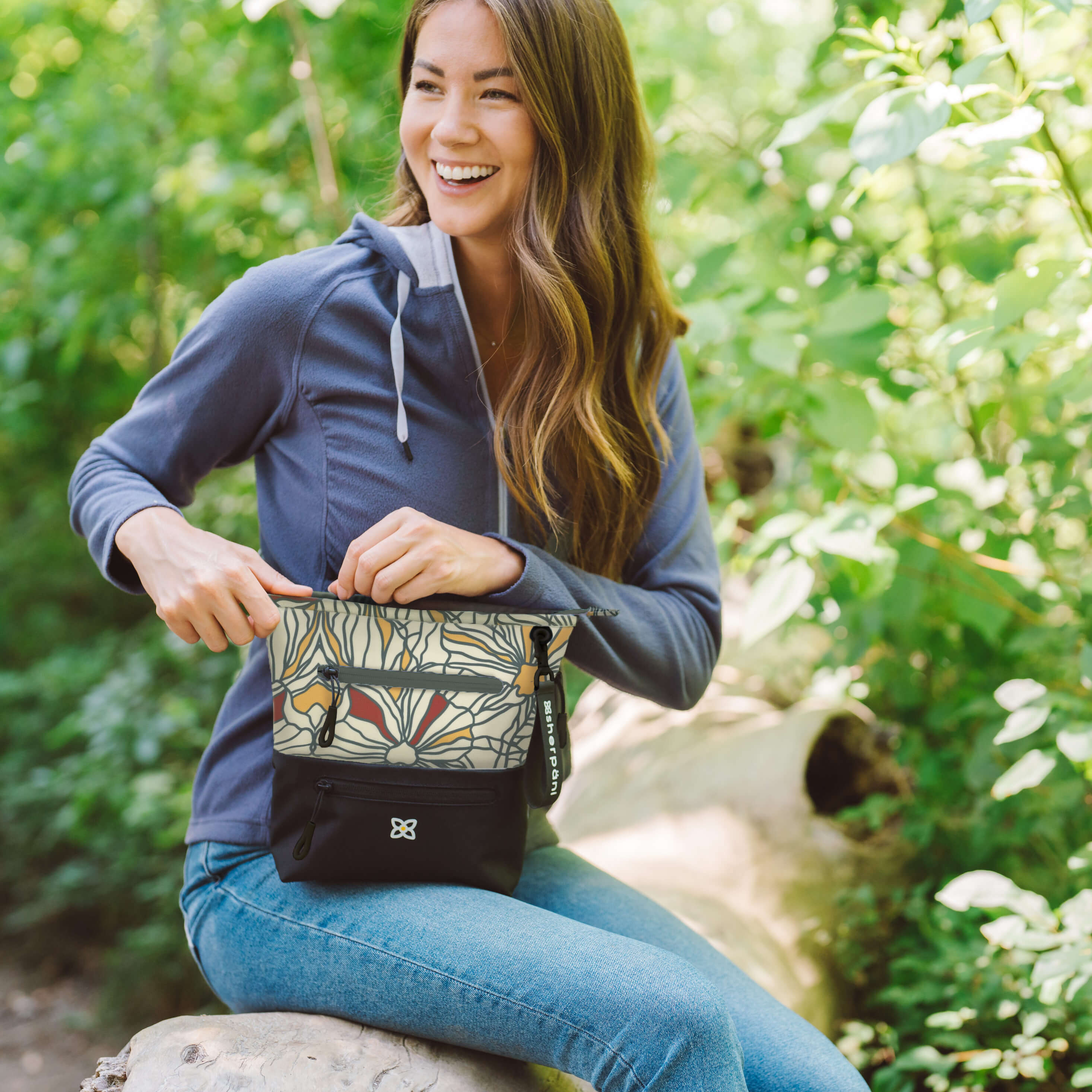 A woman sits outside in a natural setting. She is carrying Sherpani eco friendly purse with RFID blocking, the Sadie in Fiori. 